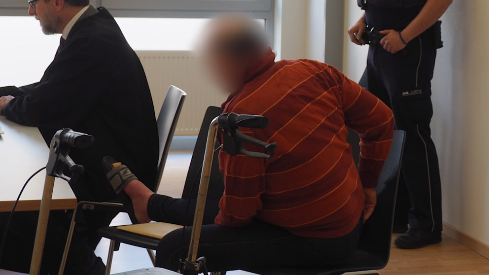 Während der Verhandlung legte er sein Bein auf einen Stuhl. Er trug nur Badeschlappen und stützte sich auf einen Rollator