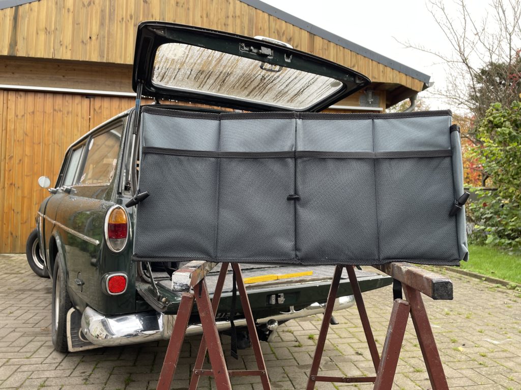 Kofferraum-Organizer auf zwei Böcken gelagert. Im Hintergrund ein Auto mit offener Kofferraumklappe.