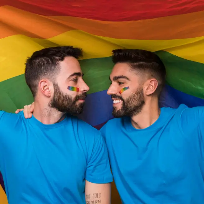 Ein männliches Paar, das sich ansieht, hinter ihnen eine Regenbogenflagge.