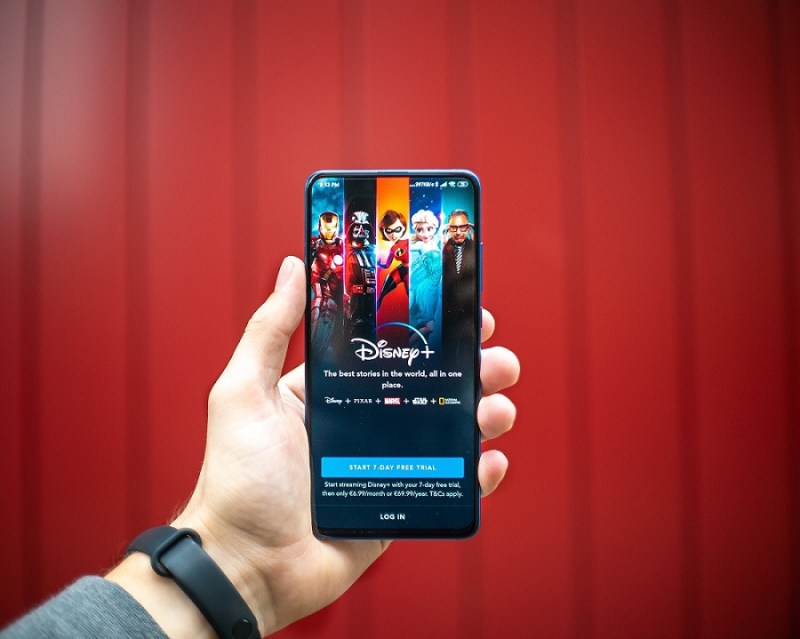 Hand hält Handy mit Auswahl von Disney+ Filmen wie Marvel