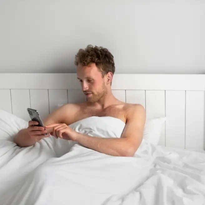 Ein Mann liegt im Bett und schaut auf sein Handy.