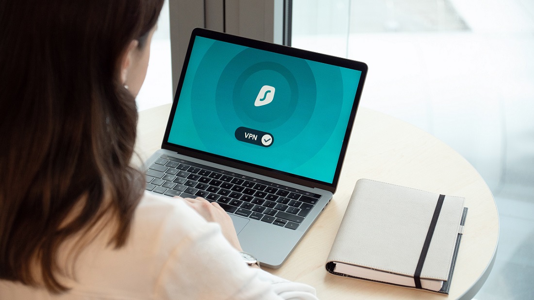 Frau sitzt vor Laptop und siehr Startbildschirm von Surfshark VPN