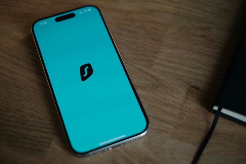 Smartphone mit Surfshark-Logo auf Holztisch. Symbolbild für Surfshark One+ Abo